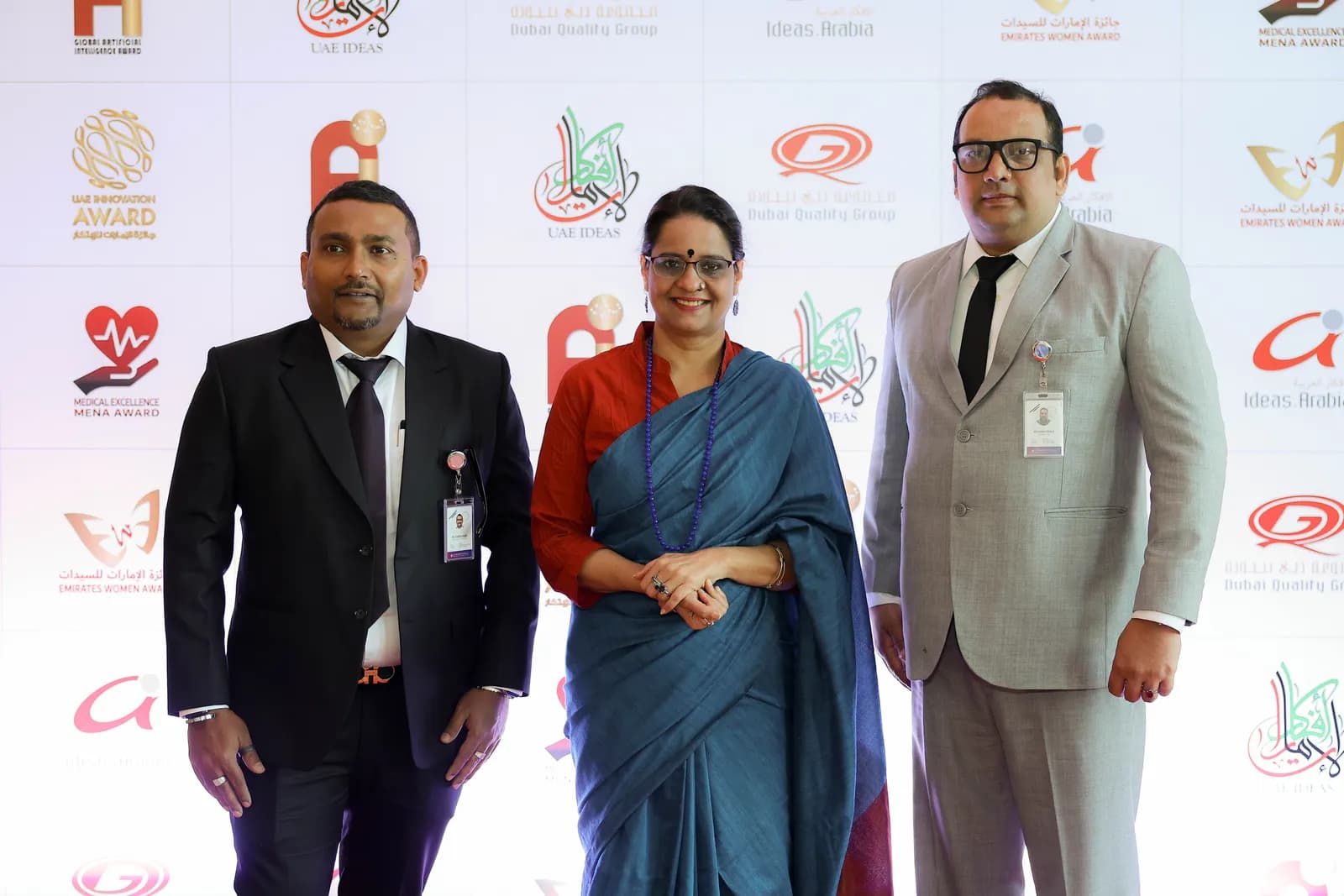 Three people posing in front of a sponsors’ photo wall