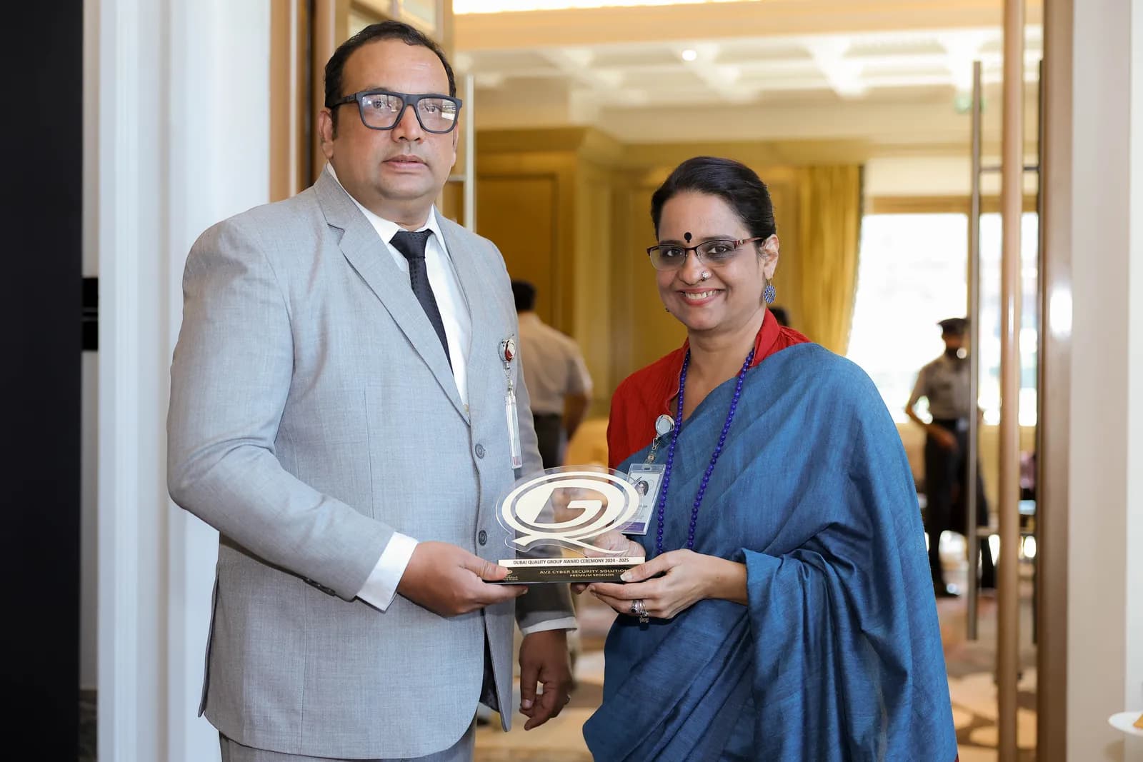 A man in a grey suit presenting a commemorative plaque to a woman in a blue sari